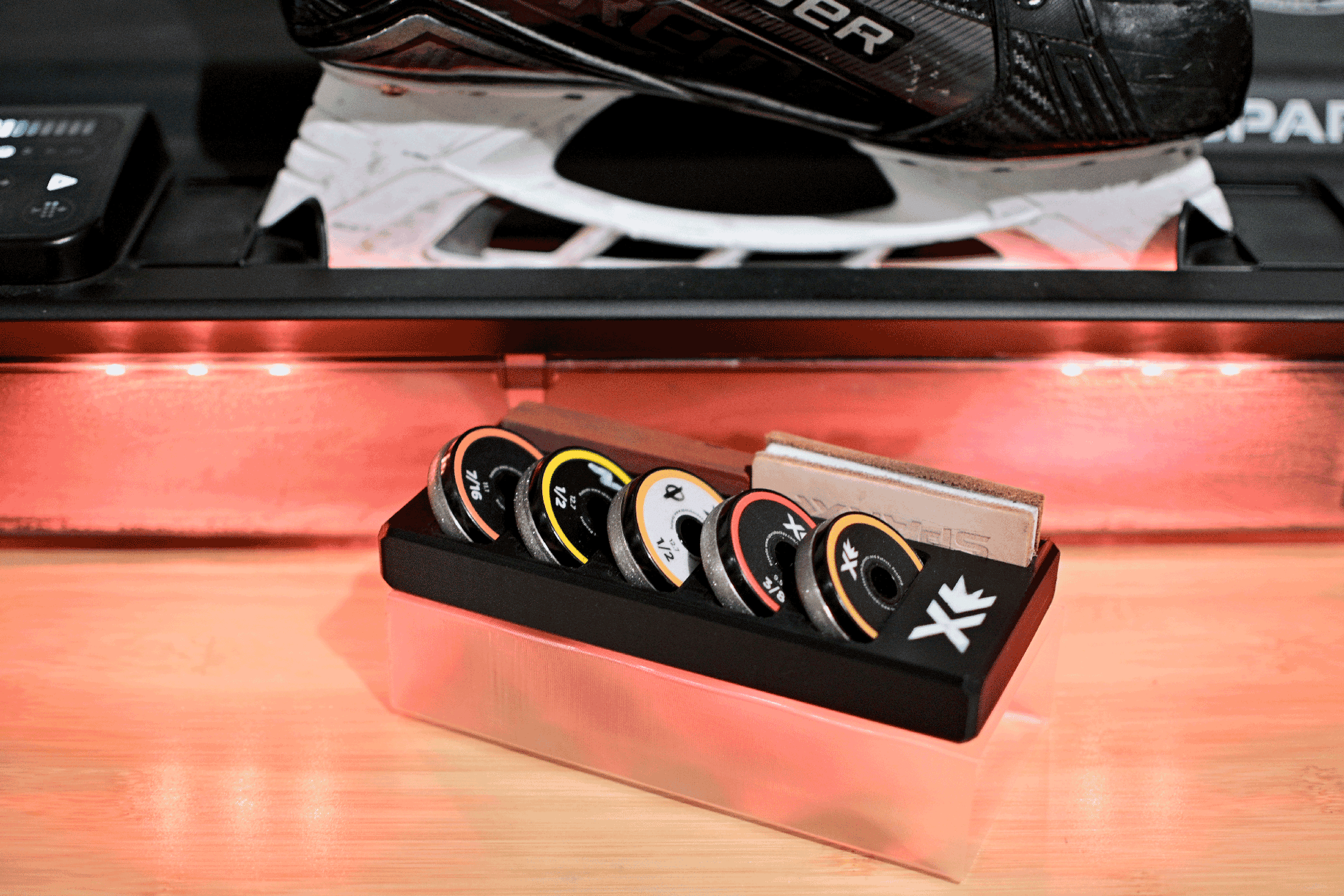 Sparx Grinding Ring Organizer with five grinding rings and a leather honing strip displayed alongside a skate blade, showcasing a complete skate sharpening setup.