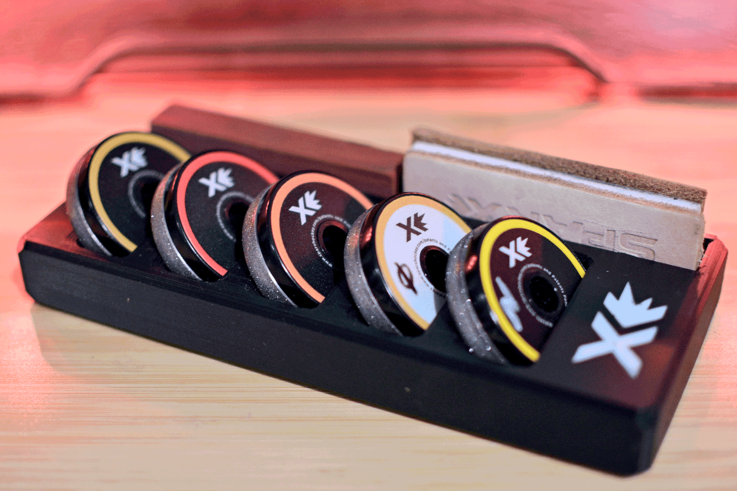 Sparx Grinding Ring Organizer holding five colorful grinding rings on a sleek black tray with a leather honing strip in the background, designed for efficient and organized skate sharpening.